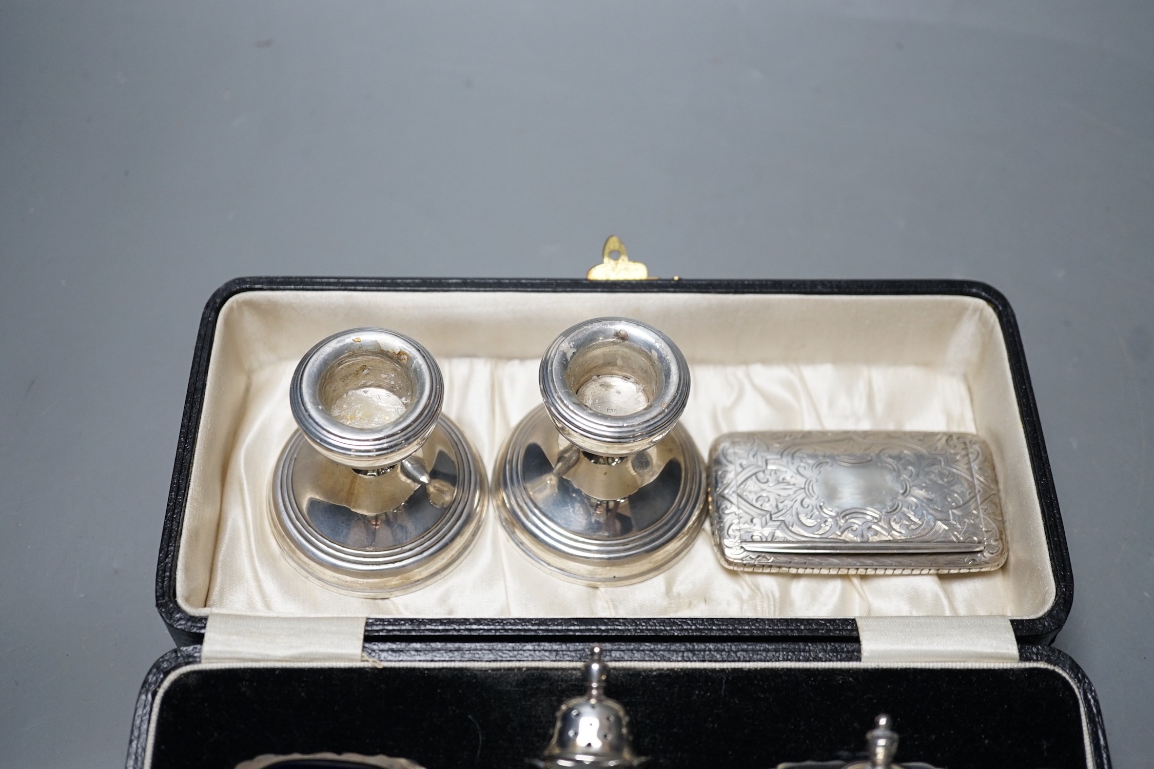 A cased George V silver three piece condiment set, Birmingham, 1930, a Victorian engraved silver snuff box, a pair of silver mounted dwarf candlesticks and a silver handled cake slice.
